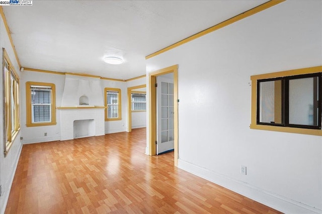 unfurnished living room with a brick fireplace, ornamental molding, and light hardwood / wood-style flooring