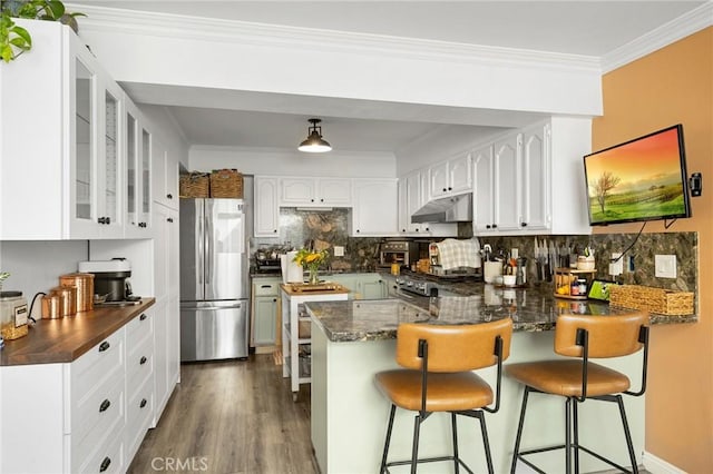 kitchen featuring ornamental molding, under cabinet range hood, stainless steel fridge, a peninsula, and dark wood-style flooring