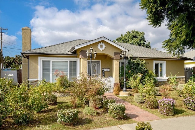 single story home with stucco siding, a chimney, and roof with shingles