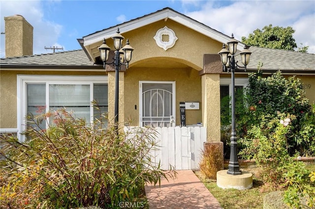 property entrance with stucco siding, a chimney, and a shingled roof