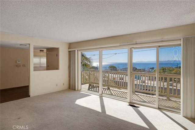 unfurnished room with a water view, carpet flooring, and a textured ceiling