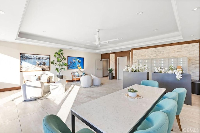 tiled dining space with ceiling fan and a tray ceiling