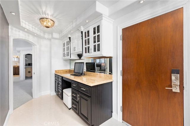 kitchen featuring light carpet, a tray ceiling, white cabinets, built in desk, and light stone counters