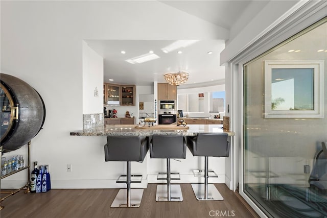 kitchen featuring dark hardwood / wood-style floors, a notable chandelier, kitchen peninsula, a breakfast bar area, and light stone counters