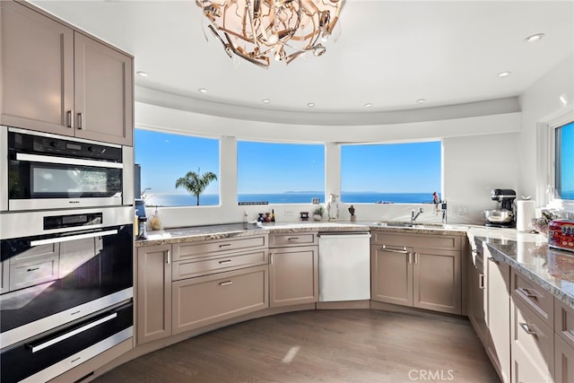 kitchen with light hardwood / wood-style floors, stainless steel double oven, dishwasher, light stone countertops, and a water view