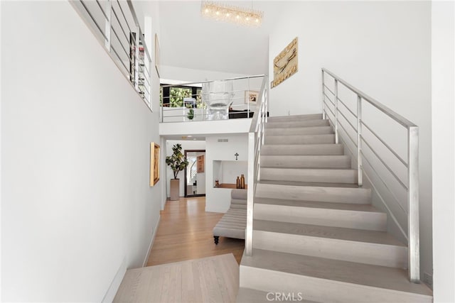 stairs with a towering ceiling, a notable chandelier, and hardwood / wood-style floors