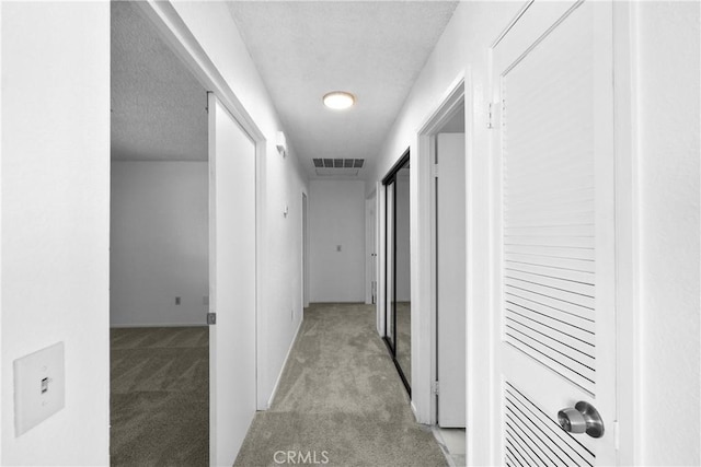 corridor with a textured ceiling and light carpet