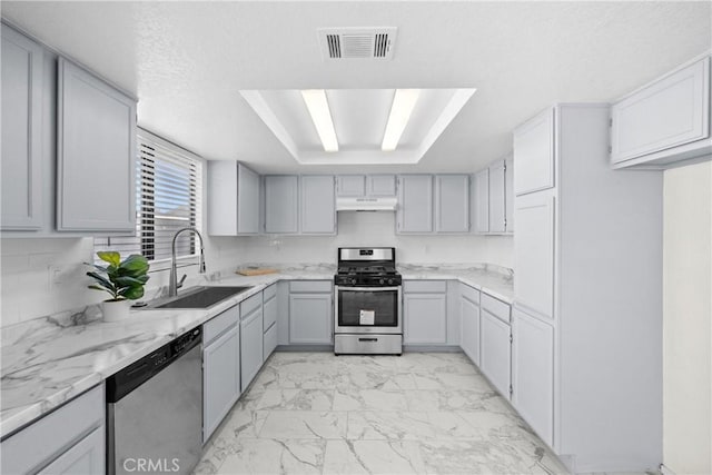 kitchen with stainless steel appliances, gray cabinetry, light stone counters, and sink