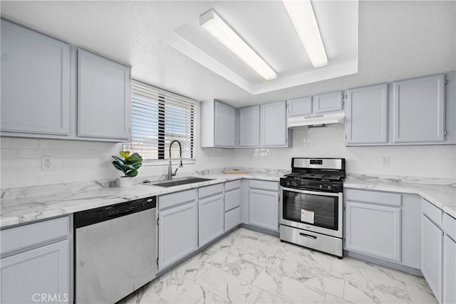 kitchen with light stone countertops, appliances with stainless steel finishes, tasteful backsplash, sink, and a raised ceiling