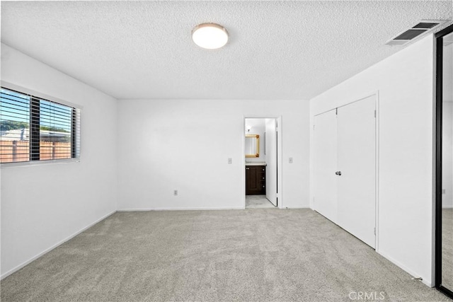 unfurnished bedroom with ensuite bathroom, light colored carpet, a closet, and a textured ceiling