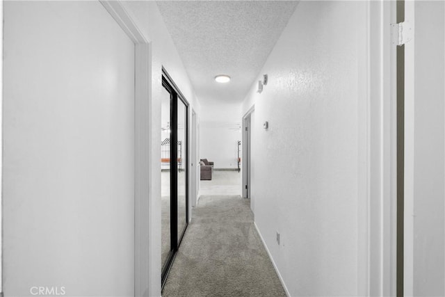 hallway featuring light colored carpet and a textured ceiling