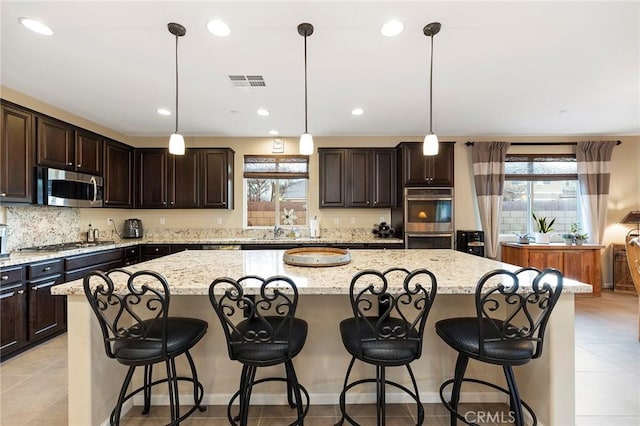 kitchen featuring hanging light fixtures, stainless steel appliances, a center island, light stone countertops, and a kitchen bar