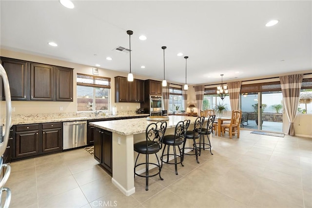 kitchen featuring a breakfast bar area, appliances with stainless steel finishes, a kitchen island, pendant lighting, and light stone countertops