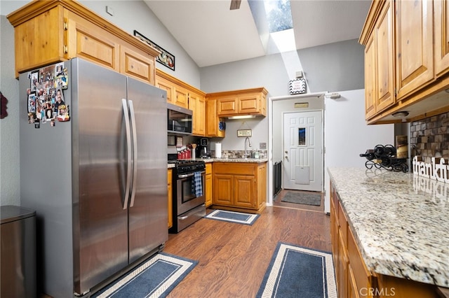 kitchen featuring vaulted ceiling, dark wood-type flooring, light stone counters, and stainless steel appliances