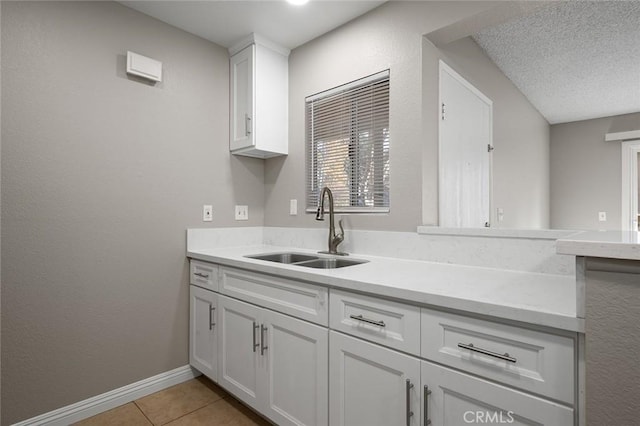 kitchen featuring a textured ceiling, light tile patterned flooring, white cabinets, and sink