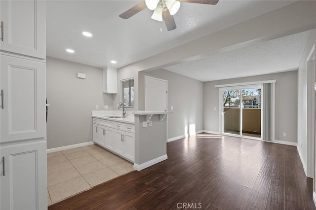 kitchen with ceiling fan, kitchen peninsula, sink, light wood-type flooring, and white cabinets