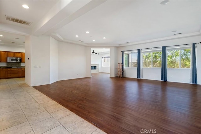 unfurnished living room featuring ceiling fan, light tile patterned floors, and a tray ceiling