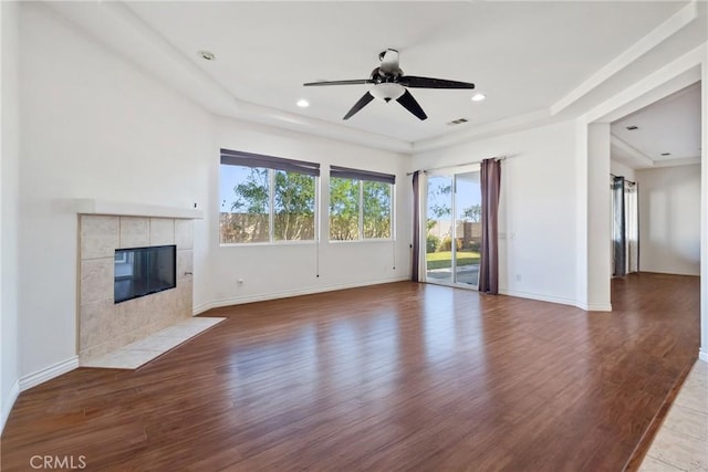 unfurnished living room with ceiling fan, hardwood / wood-style flooring, a tile fireplace, and a tray ceiling