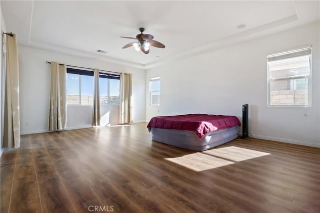 unfurnished bedroom featuring ceiling fan, dark hardwood / wood-style flooring, and a tray ceiling