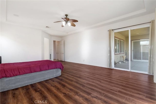 bedroom featuring ceiling fan, access to exterior, dark hardwood / wood-style floors, and a tray ceiling