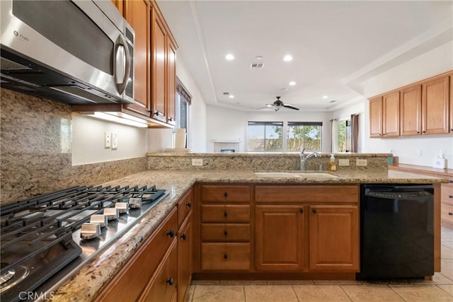 kitchen featuring kitchen peninsula, ceiling fan, appliances with stainless steel finishes, light stone countertops, and sink