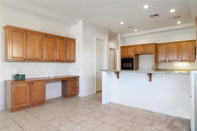 kitchen featuring built in desk, black oven, a kitchen breakfast bar, light stone counters, and light tile patterned floors