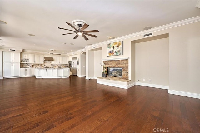 unfurnished living room with ceiling fan, dark hardwood / wood-style floors, crown molding, and a fireplace