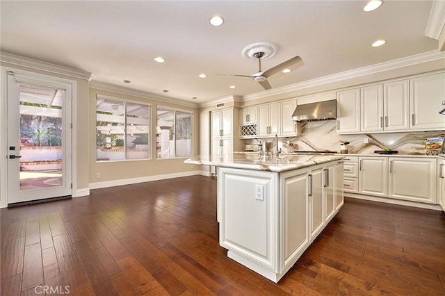 kitchen featuring white cabinetry, ceiling fan, backsplash, wall chimney range hood, and light stone counters