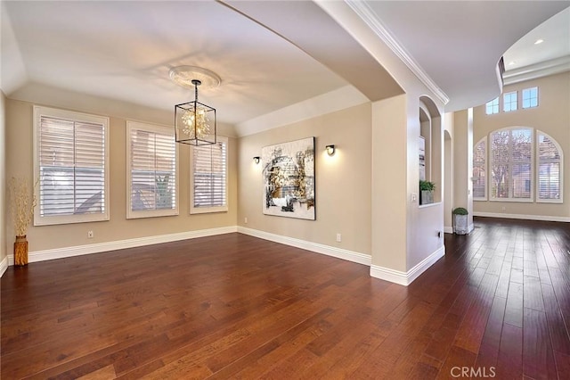 empty room with dark wood-type flooring, an inviting chandelier, and ornamental molding