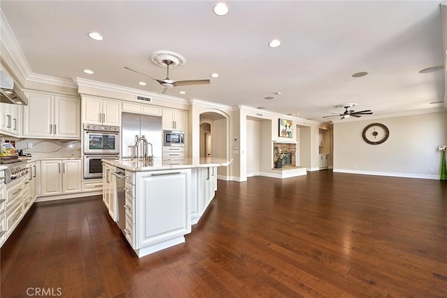 kitchen with ceiling fan, ornamental molding, an island with sink, and built in appliances