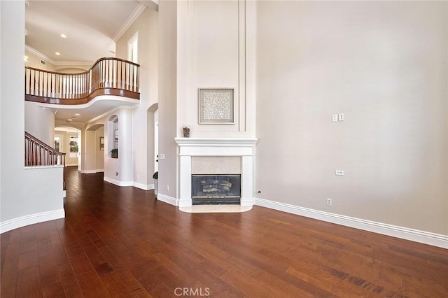 unfurnished living room featuring dark wood-type flooring, crown molding, and a high ceiling