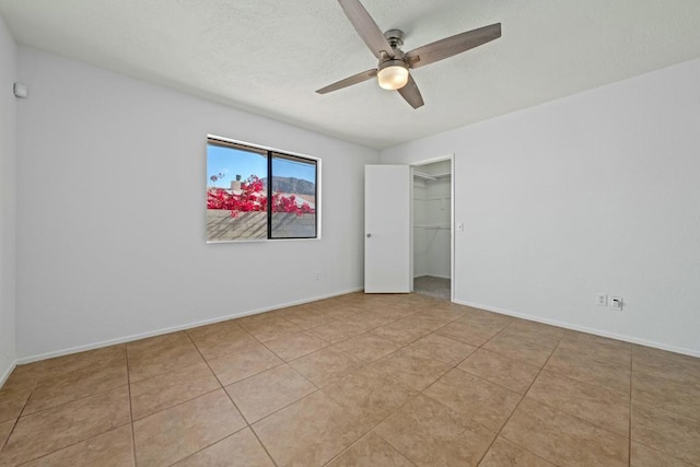 unfurnished bedroom with ceiling fan, a walk in closet, a closet, and light tile patterned floors