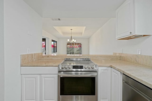 kitchen with a tray ceiling, white cabinets, appliances with stainless steel finishes, and a chandelier