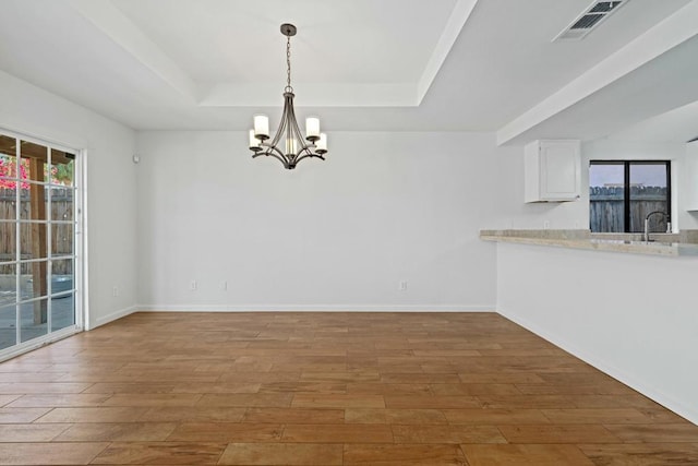 unfurnished dining area featuring an inviting chandelier, hardwood / wood-style flooring, and a tray ceiling