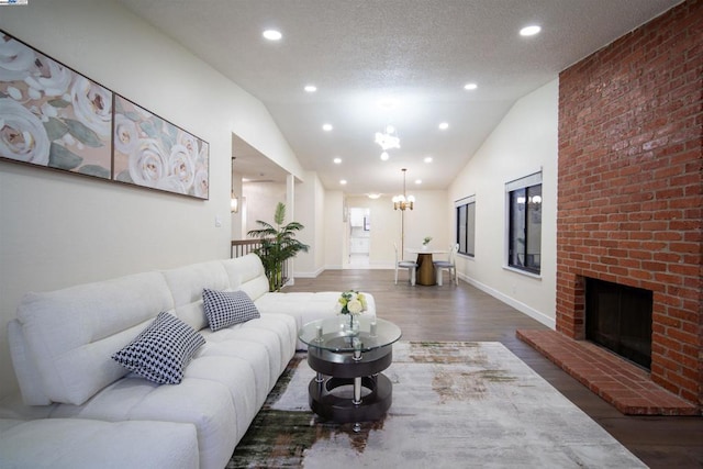 living room featuring lofted ceiling, a brick fireplace, a textured ceiling, dark hardwood / wood-style floors, and a notable chandelier