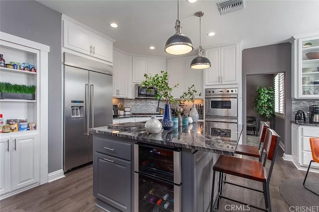 kitchen featuring a kitchen island, stainless steel appliances, white cabinets, dark stone counters, and beverage cooler