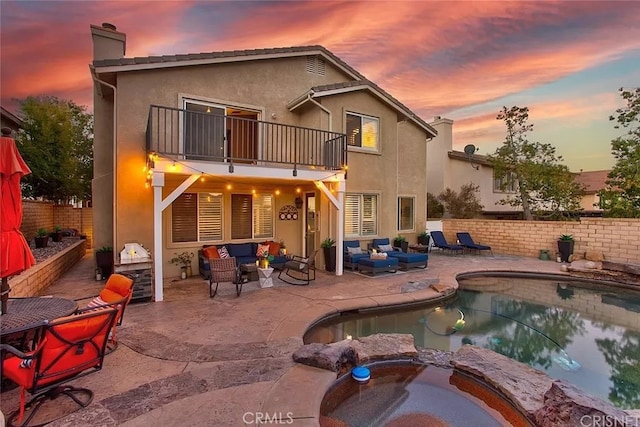 back house at dusk featuring an outdoor living space, a patio area, a pool with hot tub, and a balcony