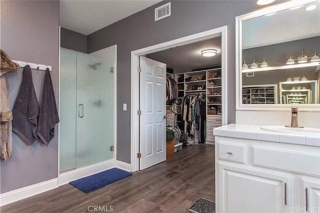 bathroom with wood-type flooring, built in shelves, a shower with door, and vanity