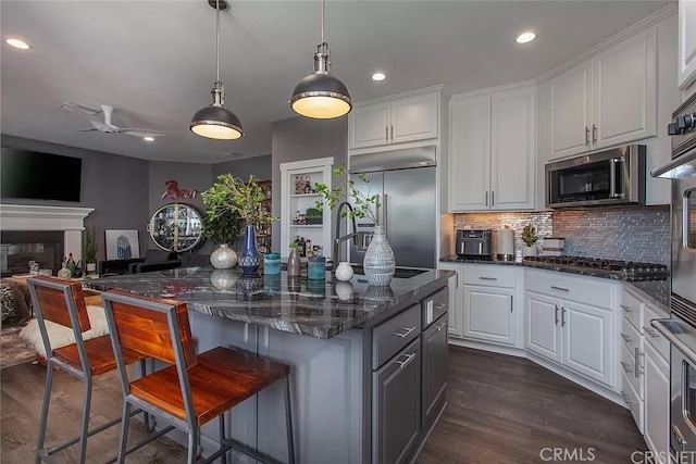 kitchen featuring appliances with stainless steel finishes, a kitchen bar, white cabinetry, dark hardwood / wood-style floors, and ceiling fan