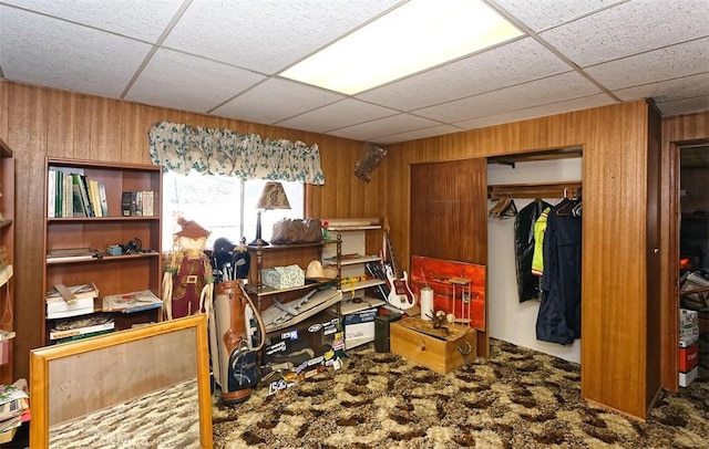 miscellaneous room with a paneled ceiling, wood walls, and carpet flooring