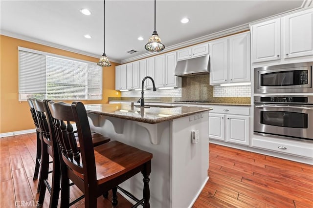 kitchen with sink, appliances with stainless steel finishes, white cabinetry, hanging light fixtures, and stone countertops