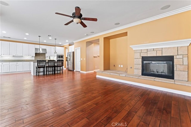 unfurnished living room with hardwood / wood-style flooring, ornamental molding, a stone fireplace, and ceiling fan