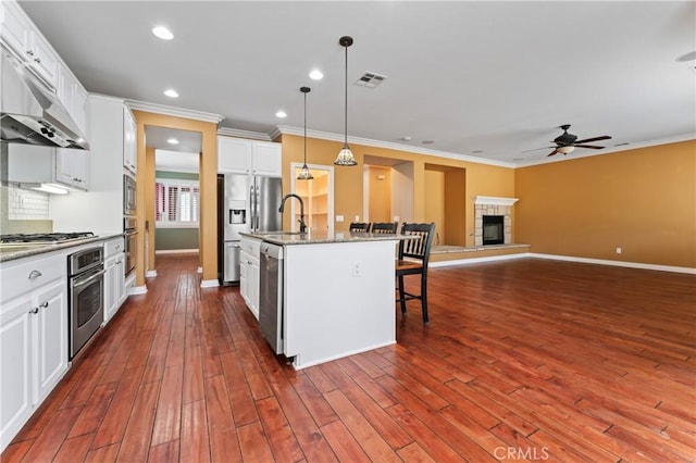 kitchen featuring a breakfast bar area, appliances with stainless steel finishes, white cabinetry, a center island with sink, and decorative light fixtures