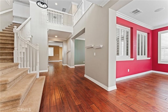 entrance foyer with ornamental molding, dark wood-type flooring, and a towering ceiling