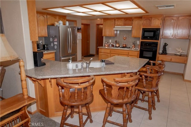 kitchen with black appliances, decorative backsplash, sink, a breakfast bar, and light tile patterned floors