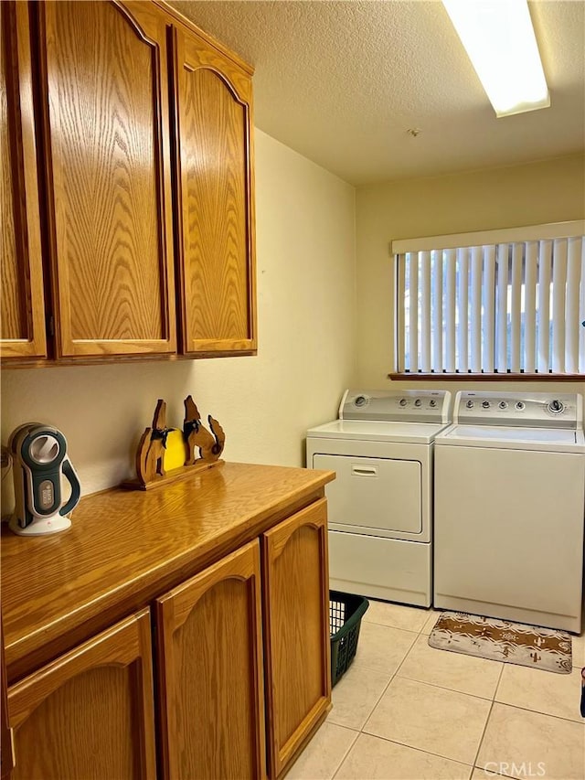 laundry room featuring light tile patterned floors, washing machine and dryer, a textured ceiling, and cabinets