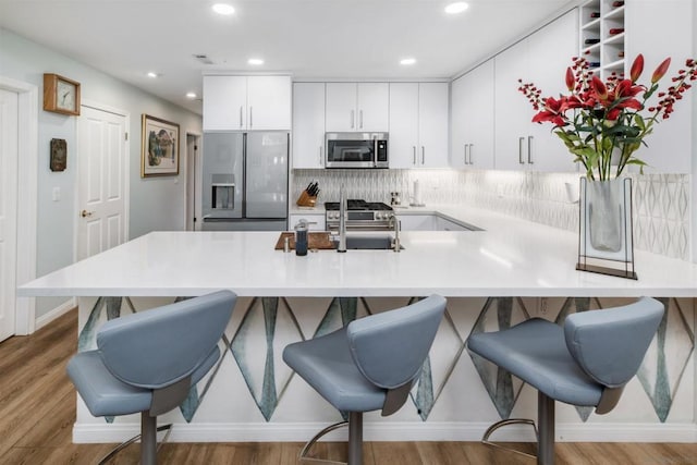 kitchen with appliances with stainless steel finishes, light hardwood / wood-style flooring, a kitchen breakfast bar, and kitchen peninsula