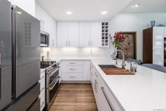 kitchen with sink, appliances with stainless steel finishes, tasteful backsplash, white cabinets, and light wood-type flooring