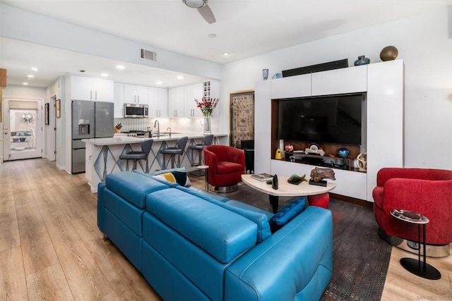 living room featuring ceiling fan, sink, and light wood-type flooring