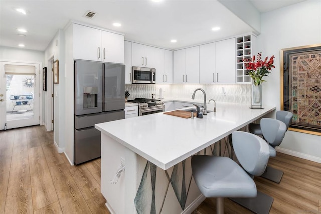 kitchen with a breakfast bar, kitchen peninsula, stainless steel appliances, decorative backsplash, and white cabinets